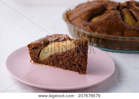 Slice of pear pie on pink plate with whole baked pie in background