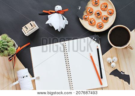 Halloween, celebration or holiday background concept : Mock up of open notebook, paper crafts, cube calendar, grilled carrots with scary face and coffee cup, Top view or flat lay with copy space