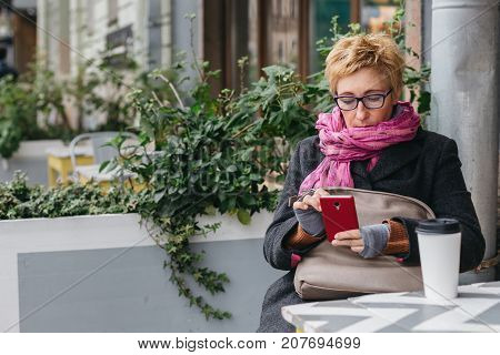 Adult pretty woman browsing smartphone in outside cafe.