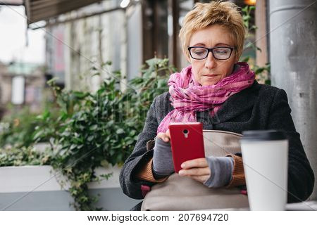 Adult pretty woman browsing smartphone in outside cafe.