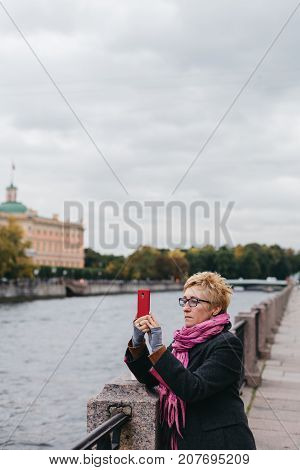 Adult woman standing on waterfront and taking shots with smartphone.