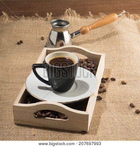 Coffee grains and cup of coffee in wooden box. Strong coffee. Coffee gezve and box on the sackcloth background. Square image