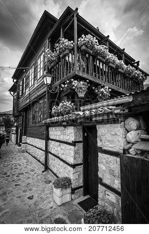 NESEBAR BULGARIA - AUGUST 21 2017: A typical residential building and a street with tourists in the old town. Nesebar is an ancient city and one of the major seaside resorts on the Bulgarian Black Sea Coast. Black and white.