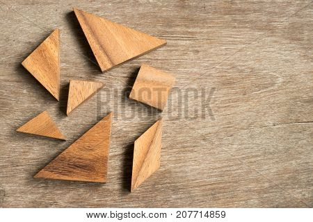 Straggled tangram puzzle wait to complete the shape on wood background