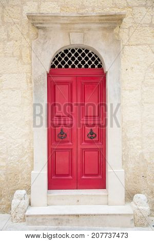 Red painted old wooden door with black iron handle in medieval city street