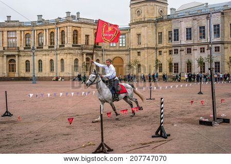 Gatchina St. Petersburg Russia - September 30 2017: Horse show of Cossacks on the parade ground of the Gatchina Palace. A Cossack in a white shirt jumps with a red flag.