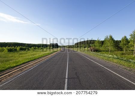 A Small Road In The Summer. The Roadway Is Divided By A White Line Of Road Markings For Traffic In V