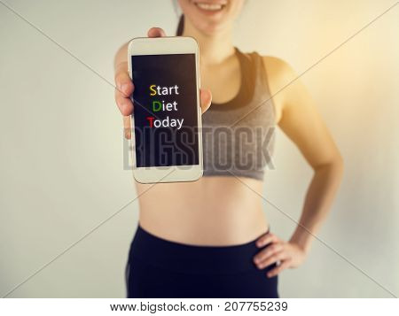 Smiling face of Young asian woman in sport bra hold smartphone tablet cell phone with start diet today message on screen. concept of diet food.