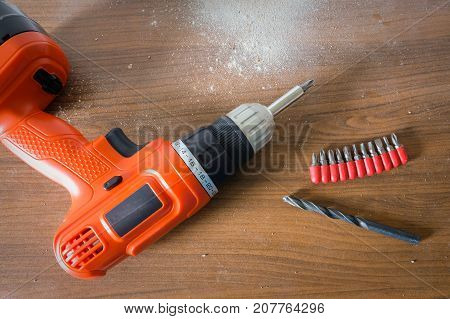 Drill machine and removable bits on wooden table with a lot of dust.