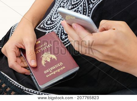 A lady holding Thailand passport while using cellphone.