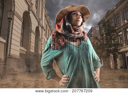 Explorer woman discovers unpopulated city . Beautiful woman wearing a cowboy hat and walking in a city covered by sand.