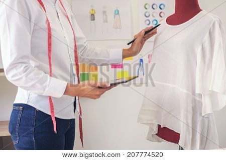 Stylish fashion designer working with measure red dummy as sketches in digital tablet of new collection in art profession and job occupation Creative Design and Artistic Concept.