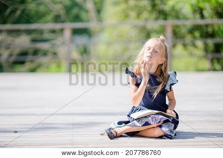 Adorable little school girl with notes and pencils outdoor.