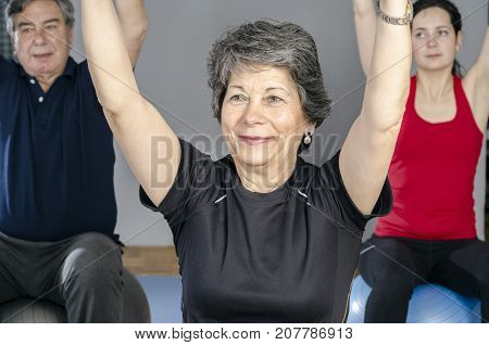 Diverse group of people a gym class sitting on Pilates ball doing ring Pilates exercise.