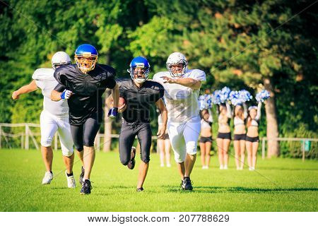 american football players running towards the goal line, cheerleaders rooting in the background