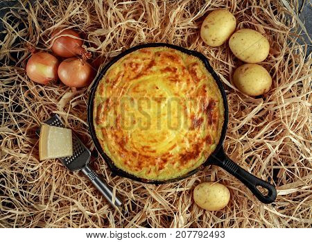 Mashed potato pie baked in rustic pan with onions and parmesan cheese on straw.