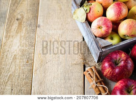Box with ripe apples and cinnamom on wooden background. Copy-space