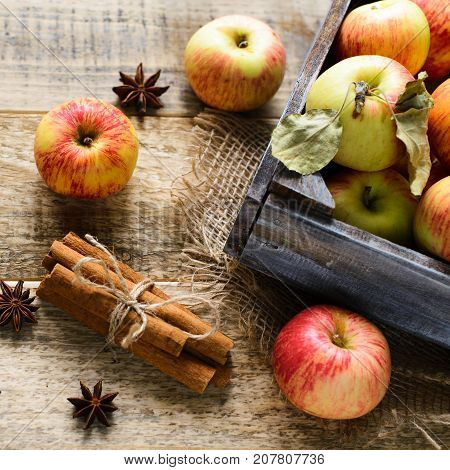 Box with ripe apples and cinnamom on wooden background. Copy-space