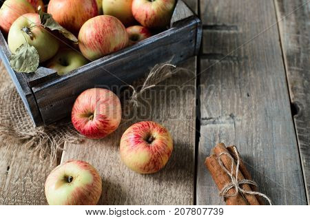Box with ripe apples and cinnamom on wooden background. Copy-space