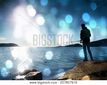 The Active Man Is Fishing On Sea From The Rocky Coast. Fisherman Check Pushing Bait On The Fishing L
