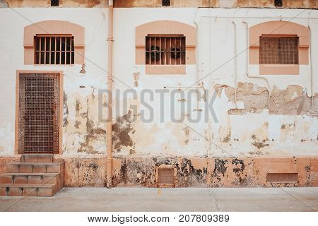 Old shabby wall with door little windows and grates looking at courtyard of prison