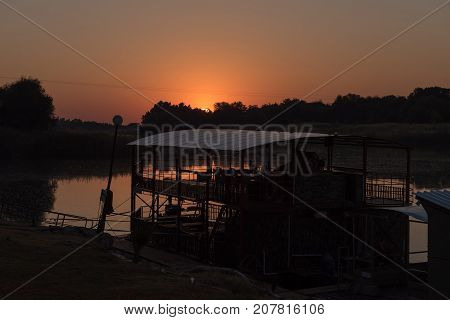 The sun is rising over Sakkie se Arkie a river boat at a holiday resort with the same name next to the Orange River at Upington