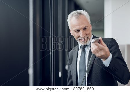 A respectable elderly man playing a mini golf in the office. He looks at the golf club and smiles.