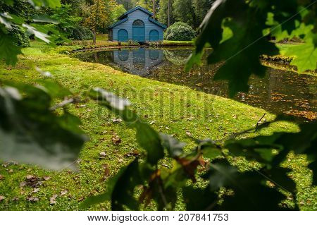 Old boat house in a tranquil ferny park with autumn leaves scattered over a charming water. A scene in the palace park 't Loo in Apeldoorn in the Netherlands