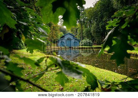 Old boat house in a tranquil ferny park with autumn leaves scattered over a charming water. A scene in the palace park 't Loo in Apeldoorn in the Netherlands