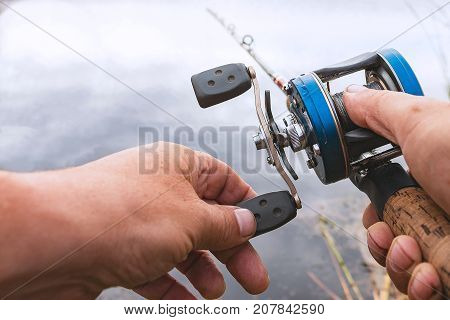 A man is fishing with a backcasting reel. Hands, a rod and a backcasting reel