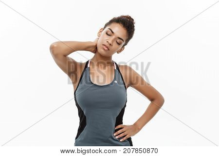 Healthy and Fitness concept - portrait of African American girl suffers a muscle injury standing holding her neck and lower back. Isolated on white background.