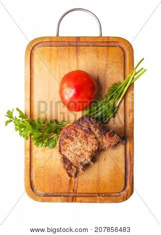 fried piece of pork with red tomato and green cocktail leaves on a wooden cutting board