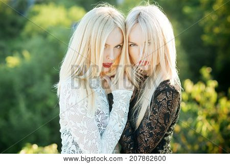 Sisters twins posing on natural landscape. Beauty and fashion. Two women with red lips and long blond hair. Dualism and dualistic nature. Contrasts and opposites concept.