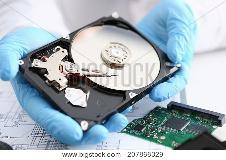 A male repairman wearing blue gloves is holding a hard drive from computer or laptop in hands. Performs fault diagnostics and performs urgent repairs recovery of lost data during deletion HDD closeup