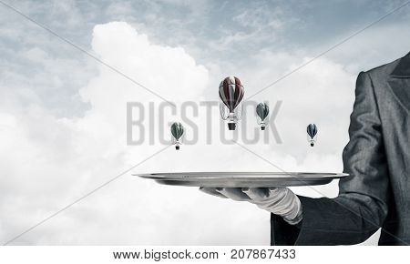 Closeup of waiter's hand in glove presenting flying aerostats on metal tray with blue cloudy skyscape on background. 3D rendering.