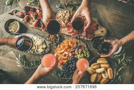 Flat-lay of friends eating and drinking together. Top view of people having party, gathering, dinner together sitting at wooden rustic table set with wine snacks and fingerfoods. Hands with glasses