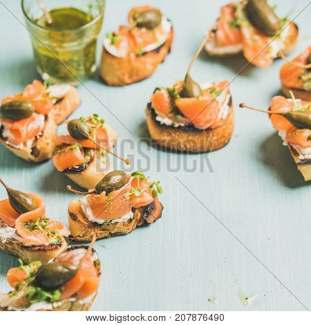 Crostini with smocked salmon, pesto sauce, watercress and capers over light blue background, selective focus, copy space, square crop. Party, catering or fingerfood concept