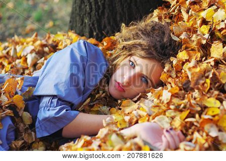 Cute young girl lying on the armful of yellow autumn
