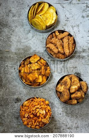 Variety of Indian snacks - Mixture Tapiyoca banana chipsSarkara varatti Sesame sticks served in metal bowls top down view