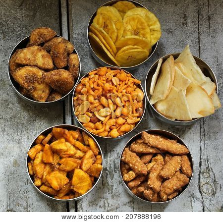 Variety of Indian snacks - Mixture Tapiyoca banana chipsSarkara varatti Sesame sticks served in metal bowls top down view