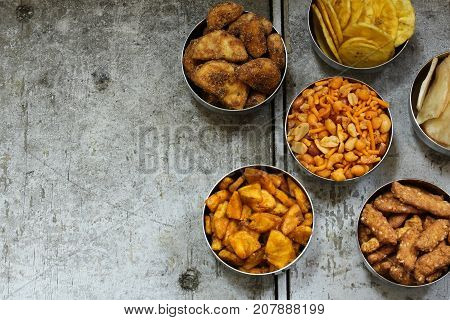 Variety of Indian snacks - Mixture Tapiyoca banana chipsSarkara varatti Sesame sticks served in metal bowls top down view