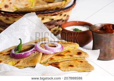 Aloo Paratha served in wooden board with raita and pickle against white background selective focus