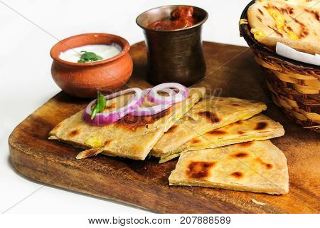Aloo Paratha served in wooden board with raita and pickle against white background selective focus