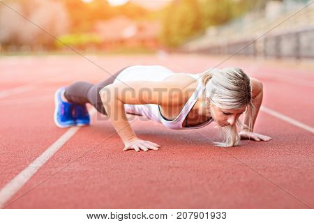 side view of young slim attractive woman doing plank exercise at outdoor stadium core training and fitness concept sun flare