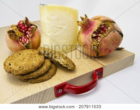 wood chopping board with assortment of cheeses cookies and pomegranate fruit. for food concept