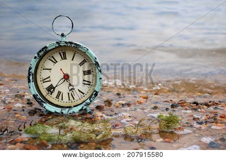 Antique alarm clock on a lakeshore in pebble covered sand