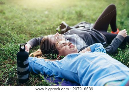 Two young sportswomen laying on grass with eyes closed relaxing after outdoor workout.