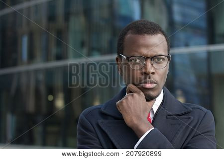 Urban Portrait Of Handsome African Businessman Dressed In Smart Coat In City Street Pressing Fist To