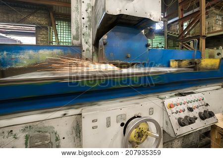Work of an industrial surface grinding machine. Grinding of a flat metal part. Sparks fly out from under the grinding wheel. Grinding with a coolant.
