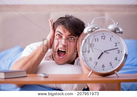 Man in bed frustrated suffering from insomnia with an alarm cloc